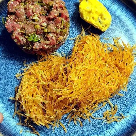 Beef tartare on a blue plate: hand-chopped raw beef with herbs, capers and mustard, a quenelle of bone-marrow sabayon, and a tangle of thin straw fries.