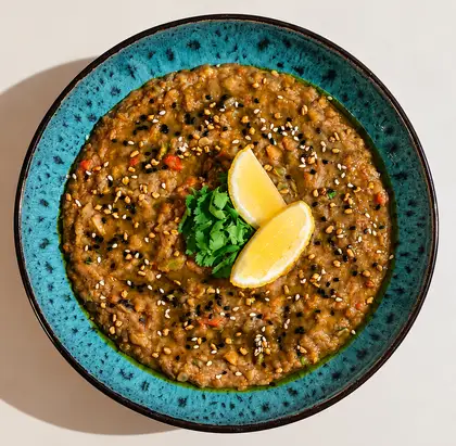 A bowl of creamy coral lentil dal garnished with fresh herbs and spices.