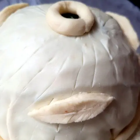 The pithivier assembled and sealed before baking: a smooth pastry dome scored in lines, with a pastry leaf on the side and a chimney at the top.