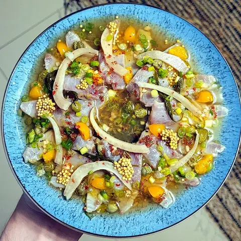 A blue-rimmed bowl of ceviche held in one hand: strips of white fish in a citrus marinade with red onion, spring onion, chilli and pieces of mango.
