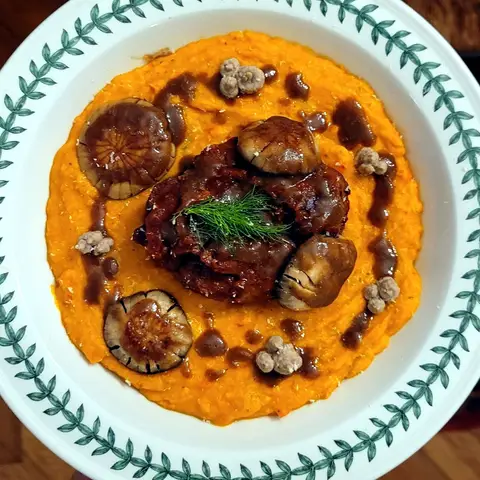 Braised veal shank in a dark, glossy sauce on a bed of orange squash purée, in a green-rimmed bowl, finished with a sprig of dill.