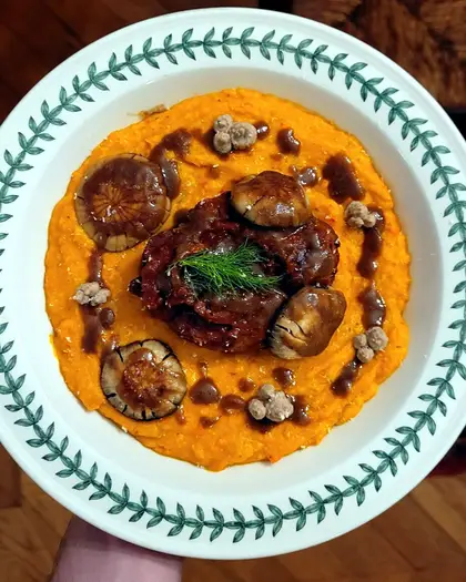 Braised veal shank in a dark, glossy sauce on a bed of orange squash purée, in a green-rimmed bowl, finished with a sprig of dill.