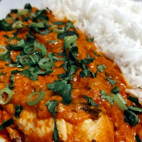 Chicken in a thick orange peanut sauce, scattered with spring onion and coriander, served beside plain white rice.