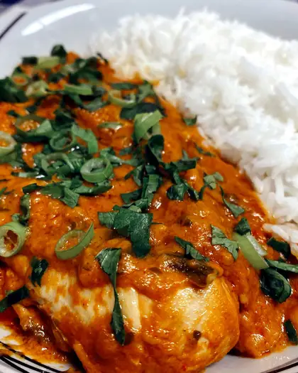 Chicken in a thick orange peanut sauce, scattered with spring onion and coriander, served beside plain white rice.