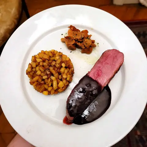 Sliced duck under a dark, glossy orange glaze on a white plate, with a round cake of diced sweet potato, browned mushrooms and a spoonful of purée.