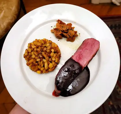 Sliced duck under a dark, glossy orange glaze on a white plate, with a round cake of diced sweet potato, browned mushrooms and a spoonful of purée.