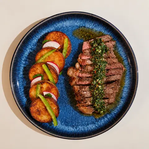 Sirloin & Potatoes on a blue plate with a drizzle of chimichuri