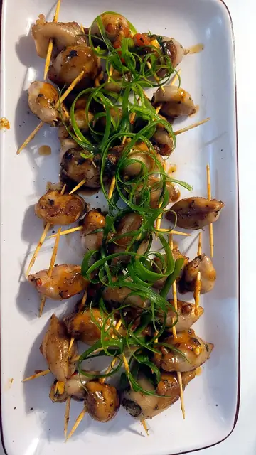 Pieces of stuffed calamari pinned with cocktail sticks on a white rectangular platter, topped with a line of shredded spring onion.