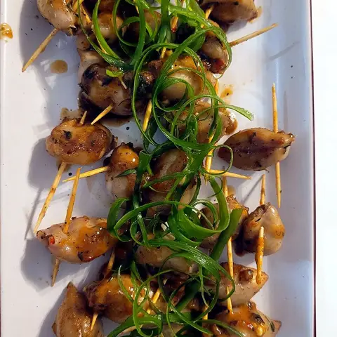 Pieces of stuffed calamari pinned with cocktail sticks on a white rectangular platter, topped with a line of shredded spring onion.