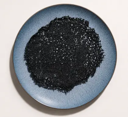A black, lace-like crispy tuile sits on a blue-gray ceramic plate against a light background.