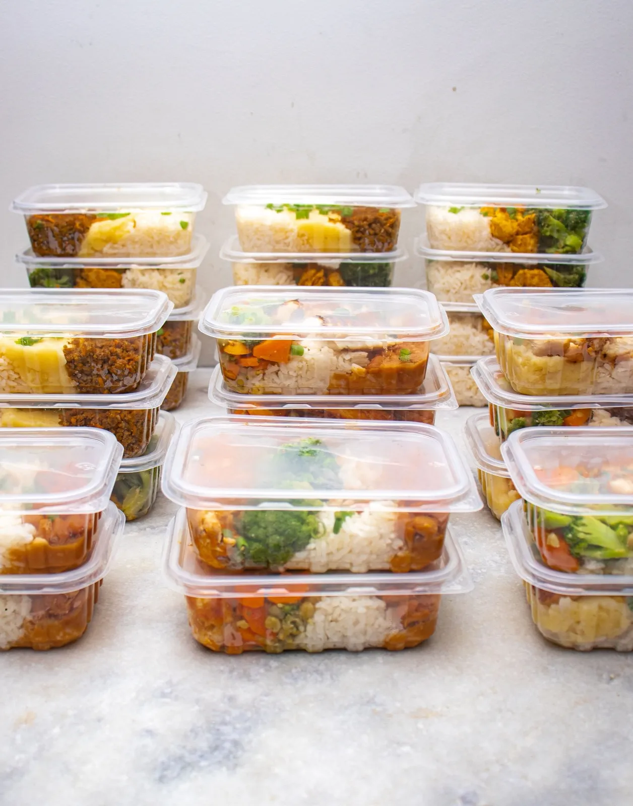 Rows of stacked takeaway-style containers packed with rice, vegetables and chicken, ready to reheat.